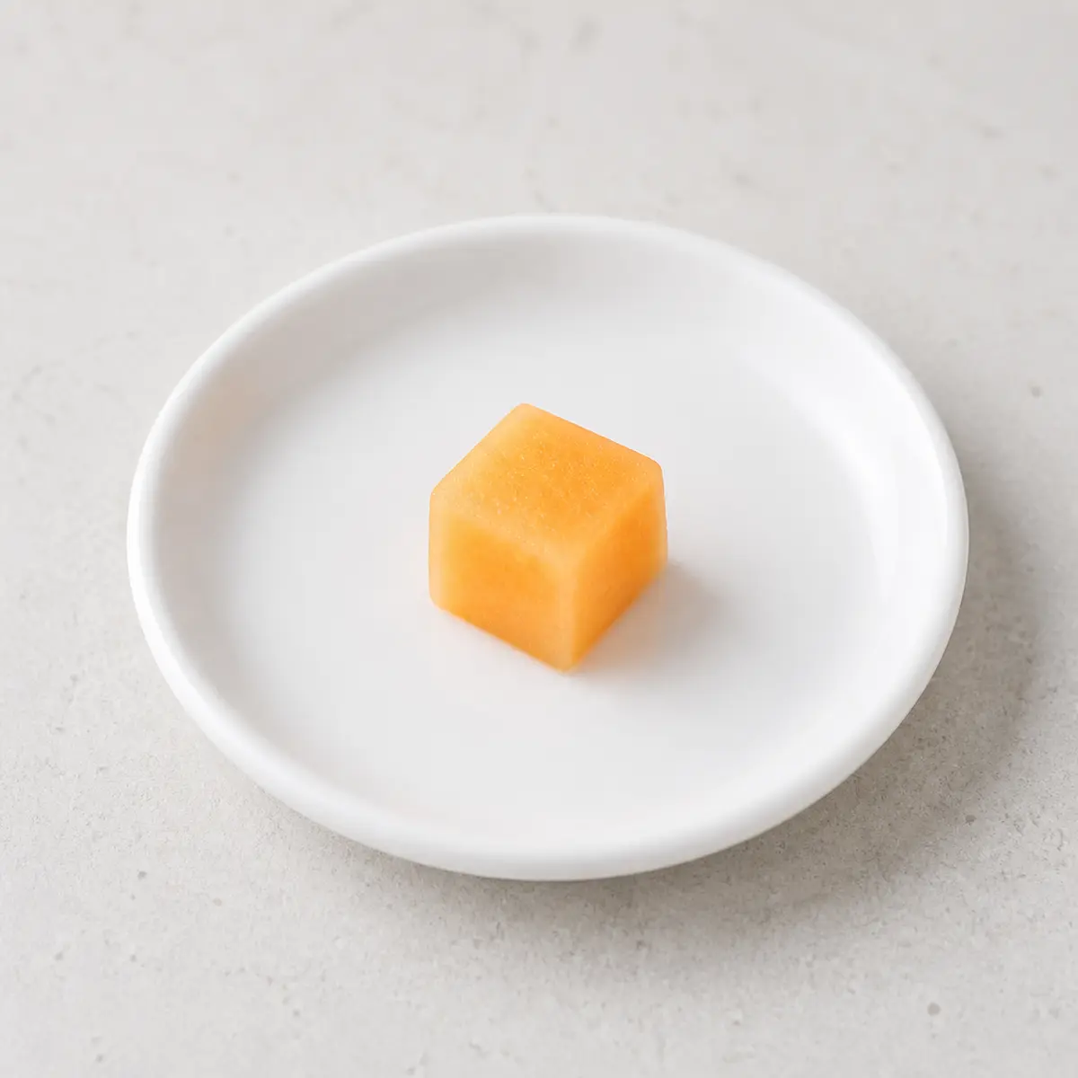 Tiny plain cantaloupe cube on a saucer