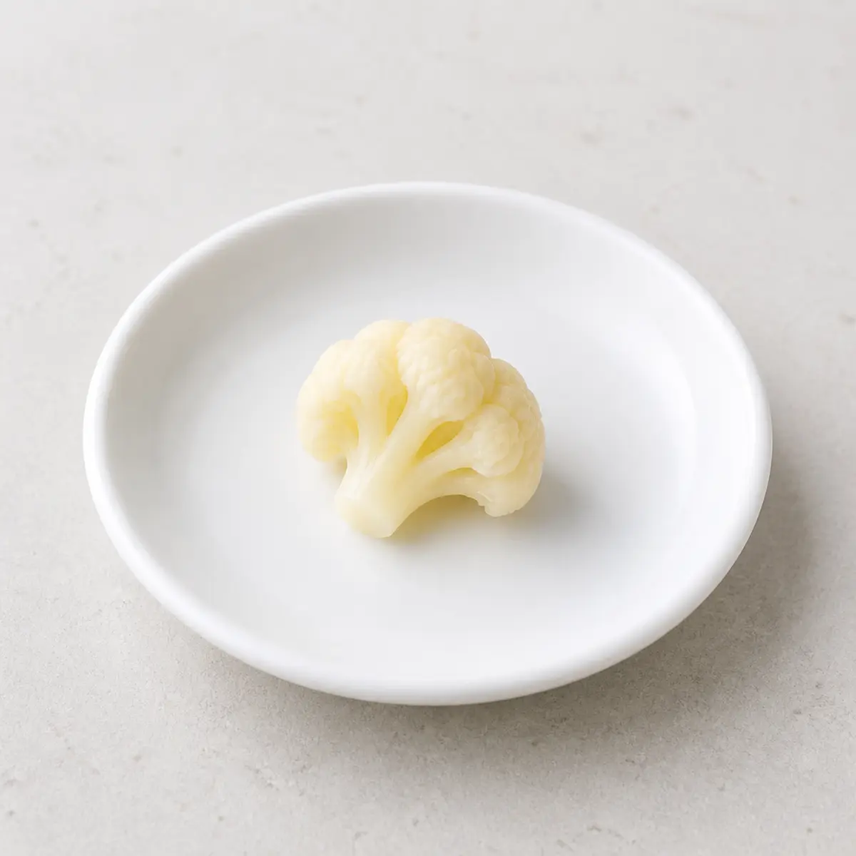 Tiny plain cooked cauliflower floret on a saucer