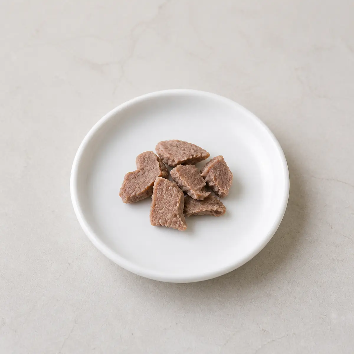 Tiny plain cooked duck pieces on a saucer