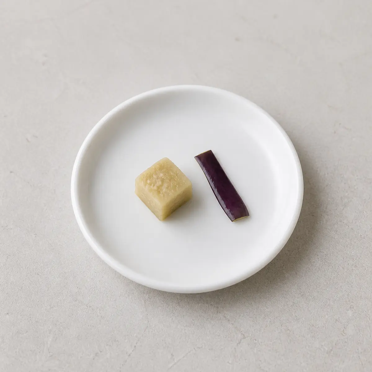Tiny cooked eggplant cube with purple peel cue on a saucer