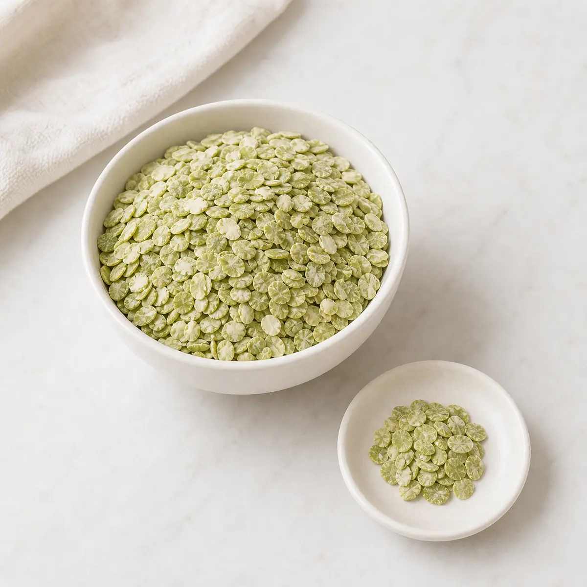 Pale green dried pea flakes in a bowl with one tiny pinch on a saucer