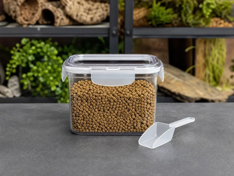 Clear airtight dry-food container with a locking lid and small scoop on a dedicated reptile supply surface.