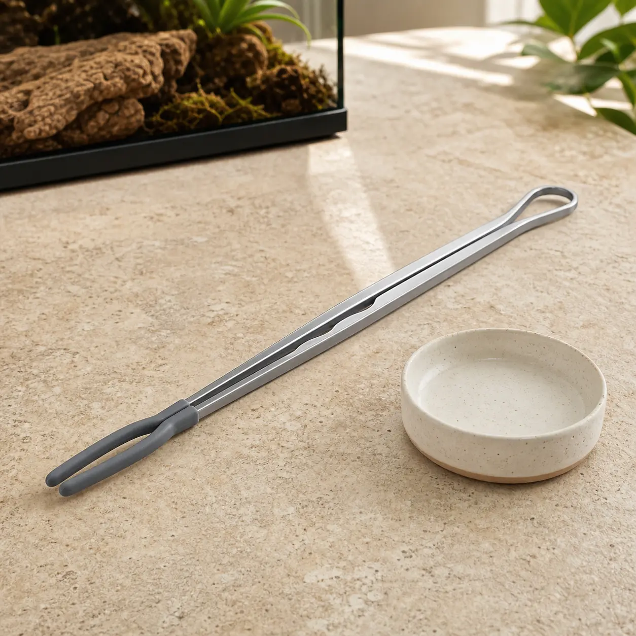 Long reptile feeding tongs staged beside a clean feeding dish.